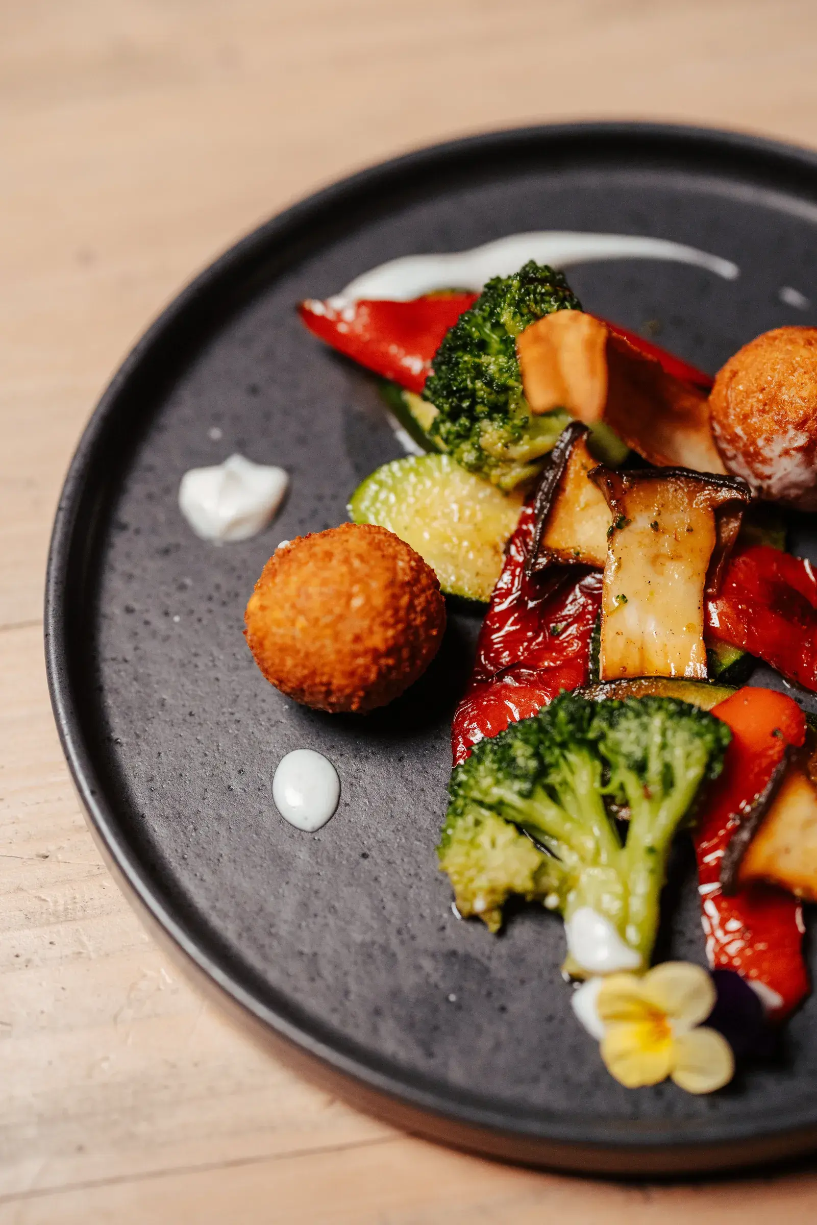 Fein angerichtetes Fastengericht mit gegrilltem Biogemüse, Broccoli und knusprigen Bällchen auf dunklem Teller