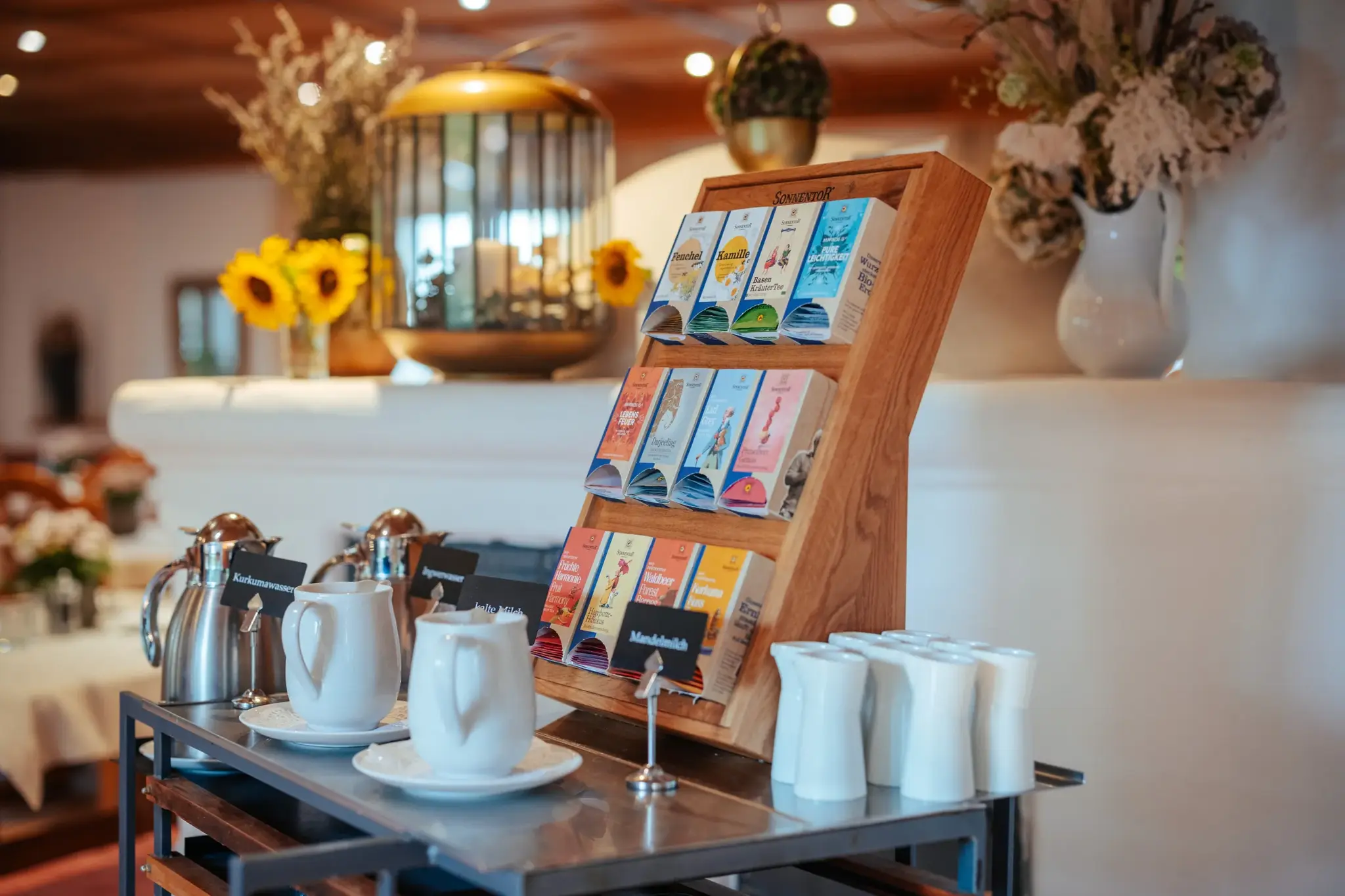 Frühstücksstation mit Bio-Kräutertees und weißen Porzellankännchen, Sonnenblumen und Trockenblumen im Biohotel Schweitzer