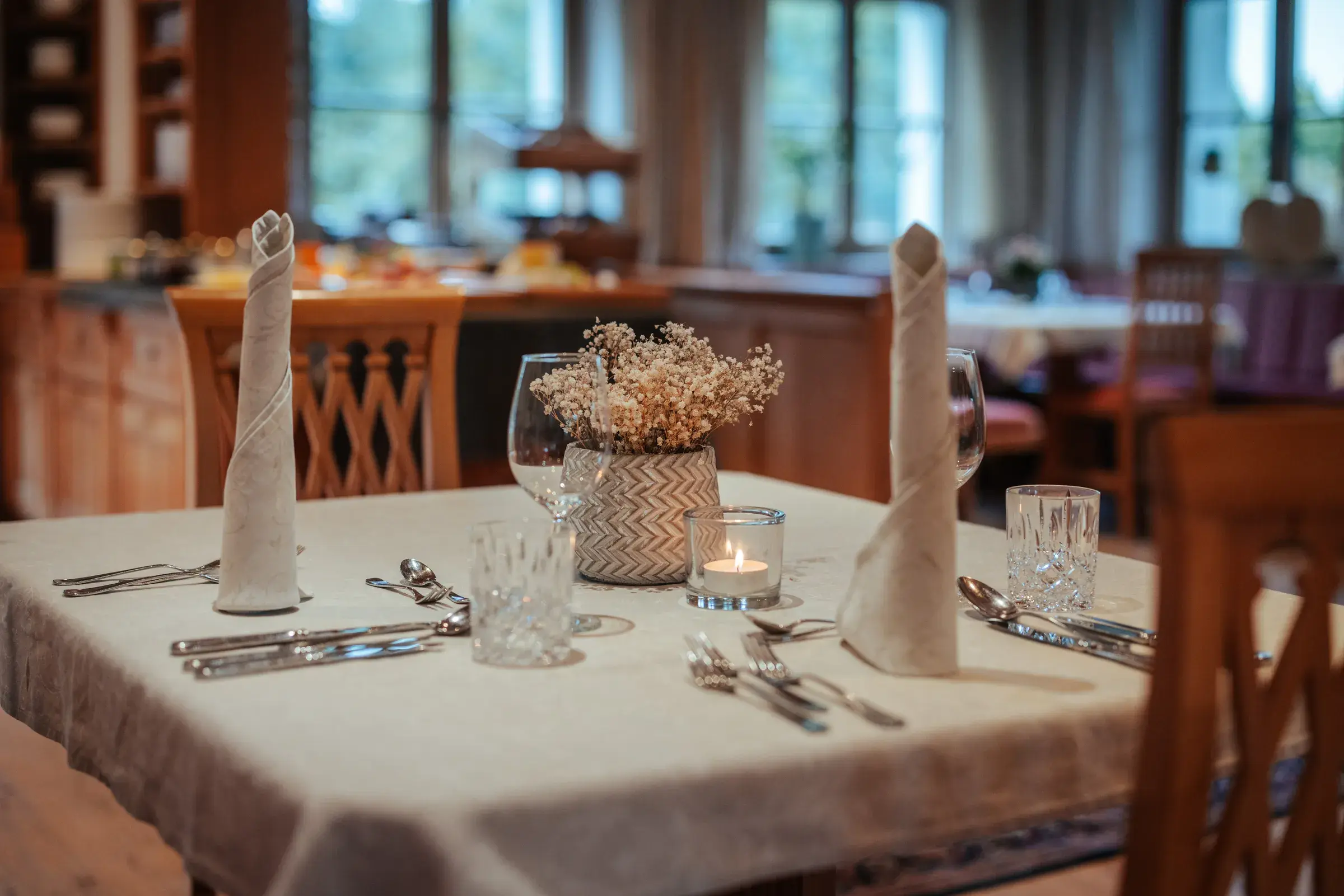 Festlich gedeckter Tisch mit gerollten Leinenservietten, Kristallgläsern und Kerzenlicht im Restaurant Greenvieh
